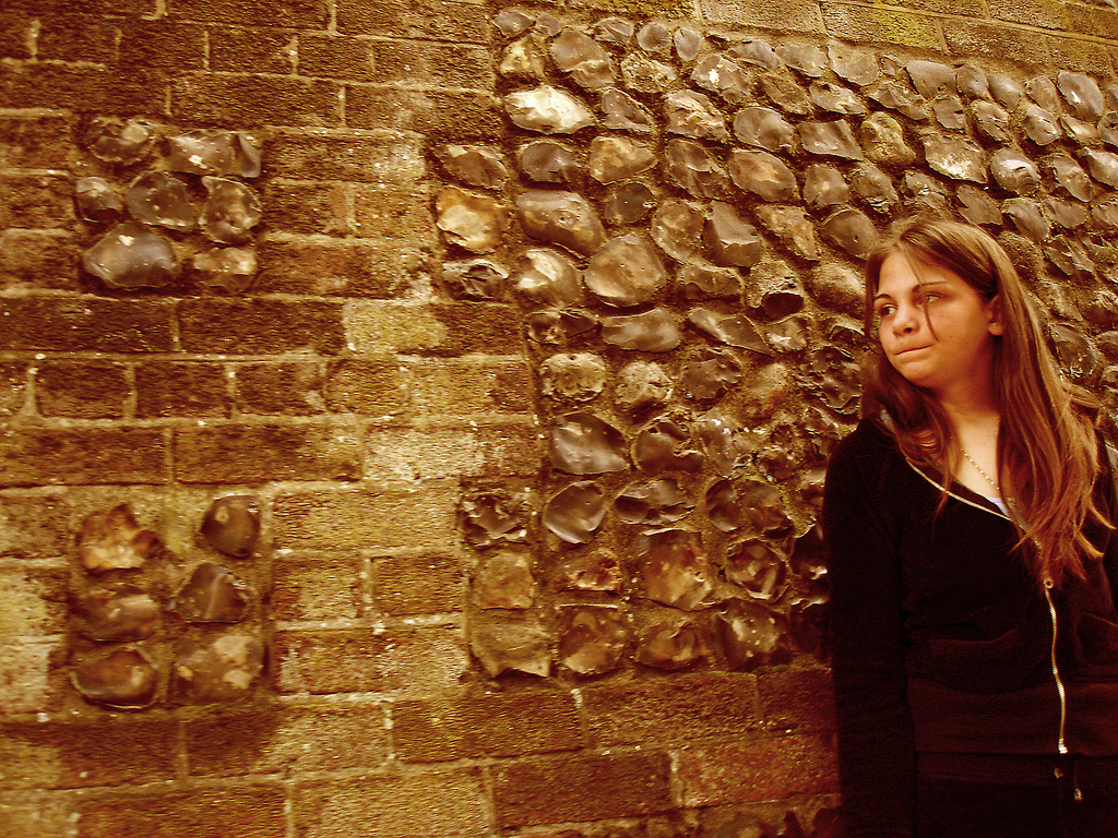 A girl standing by a stone wall, looking anxious.